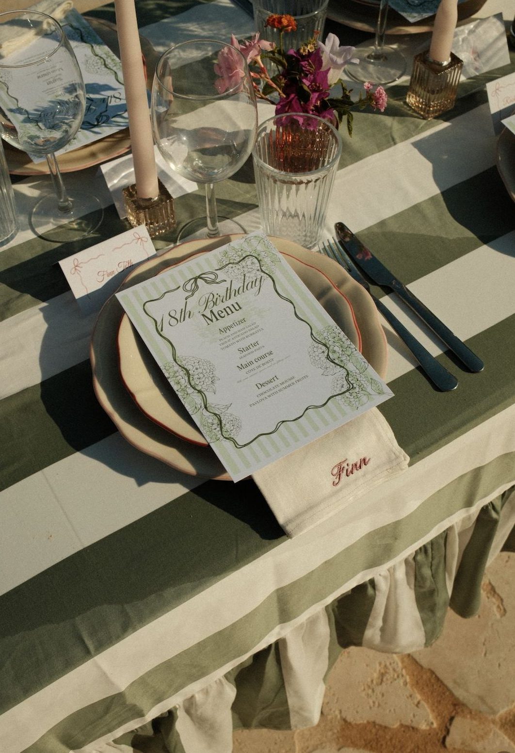 Close-up of an 18th-birthday place setting with an embroidered napkin, wine glasses and a striped birthday menu card